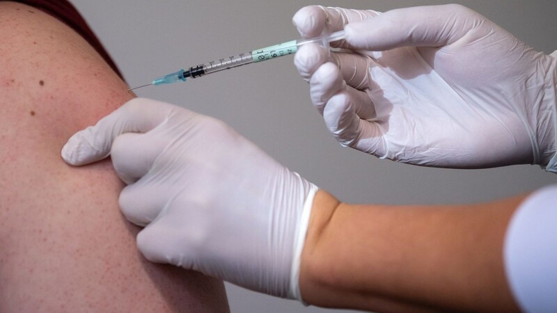 Eine Mitarbeiterin eines Impfzentrums impft einen Mann gegen Corona.