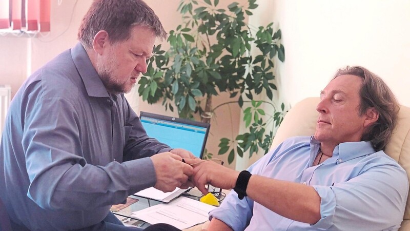 Hypnotiseur Anton Späth (links) steckt mir einen Sensor für das Biofeedback an den Zeigefinger, bevor er mich in eine absolute Entspannungsphase führt.