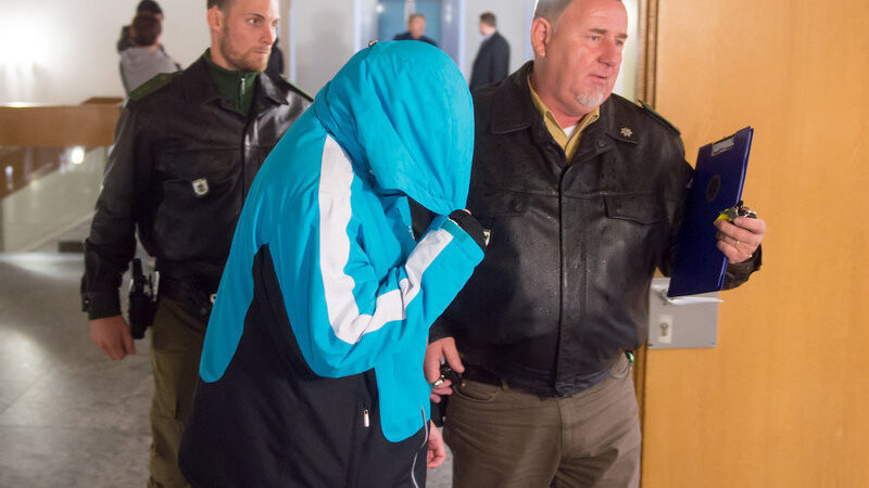 Die Angeklagte Stefanie B. (M) verbirgt am 24.05.2016 in Landshut (Bayern) im Landgericht ihr Gesicht in der Kapuze ihrer Jacke als sie von Polizisten in den Verhandlungssaal geführt wird. Im Prozess gegen eine 23-Jährige, die ein Neugeborenes mit einer Kordel erstickt und die Leiche in ihrem Auto versteckt haben soll, wird das Urteil erwartet.