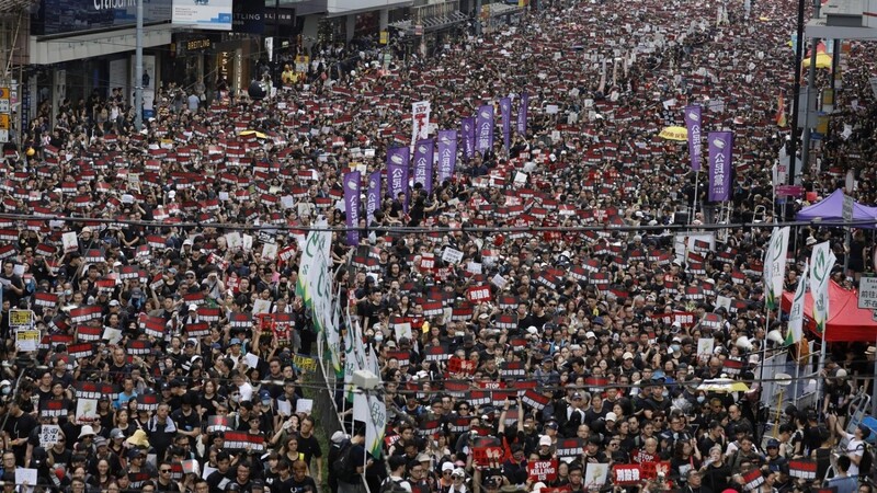 Menschen mit Regenschirmen und Protestschildern sind in Hongkong zu Hunderttausenden auf den Straßen.