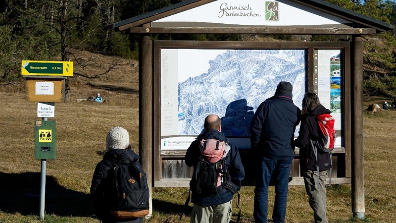 Wanderer stehen in Garmisch-Partenkirchen (Bayern) unterhalb der Kramerspitze vor einer Winterwanderkarte im Grünen.