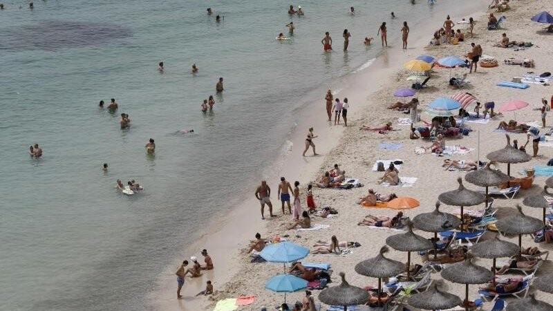 Touristen genießen an einem Strand bei Puerto Portals auf Mallorca die Sonne und das Meer. Der Klimawandel stellt die Reisebranche vor neue Herausforderungen.