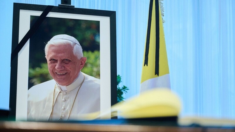 Das Kondolenzbuch für den verstorbenen emeritierten Papst Benedikt XVI.liegt auf einem Tisch vor einem Bild des Verstorbenen.
