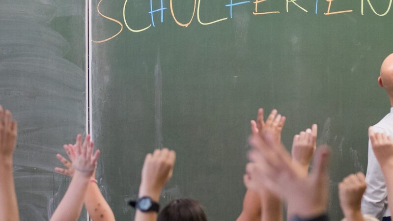 Ein Lehrer schreibt "Schulferien" an die Tafel. Manche Lehrer müssen in den Sommerferien auf Gehalt verzichten. (Symbolbild)