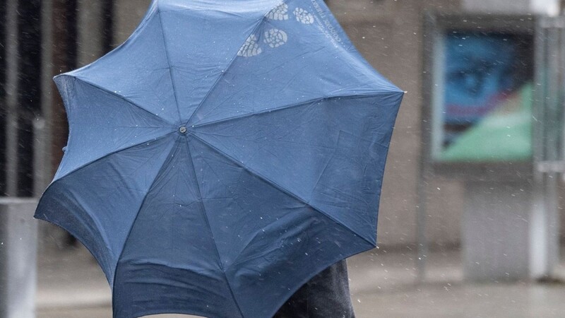 Bei Regenwetter kämpft sich ein Passant mit Regenschirm durch die Innenstadt.