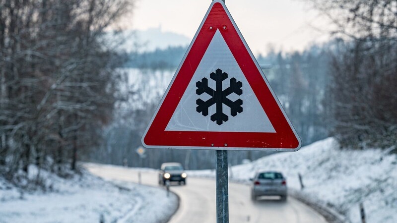 Ein Verkehrsschild mit einer Schneeflocke, das vor glatter Fahrbahn warnt steht am Straßenrand. Glatteis macht Teilen Süddeutschlands weiter zu schaffen.