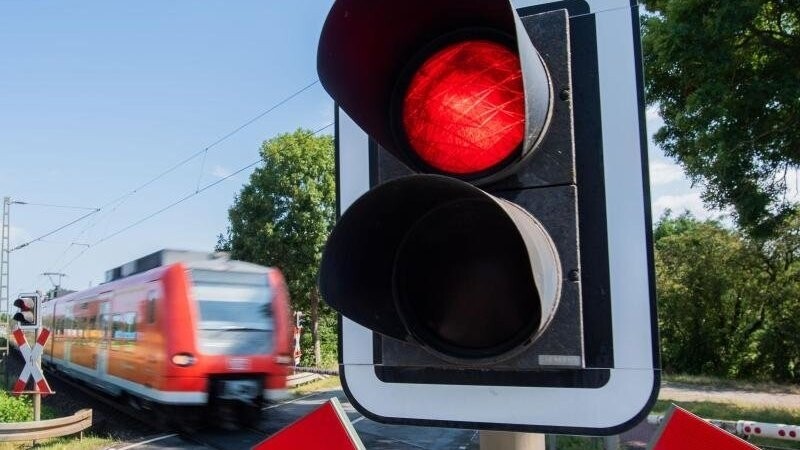 Eine S-Bahn der Deutschen Bahn (DB) fährt an einem Bahnübergang mit einer roten Ampel vorbei.