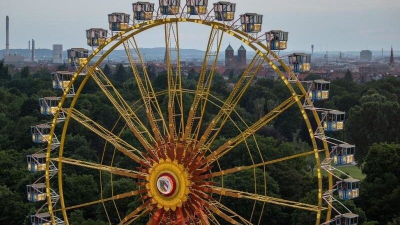 Das Riesenrad des temporären Freizeitparks "NürnBärLand" erhebt sich vor der Stadtkulisse in der Abendsonne.