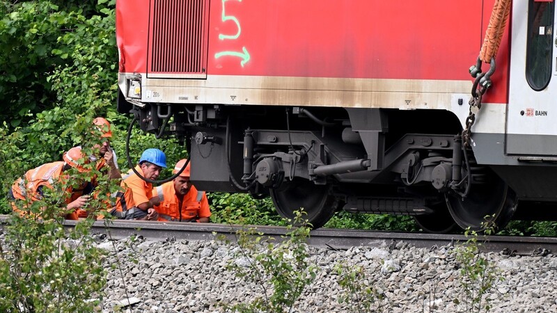 Arbeiter begutachten die Anhebung eines Waggons des verunfallten Regionalzugs, der für die Bergung an einem Schienenkran hängt.