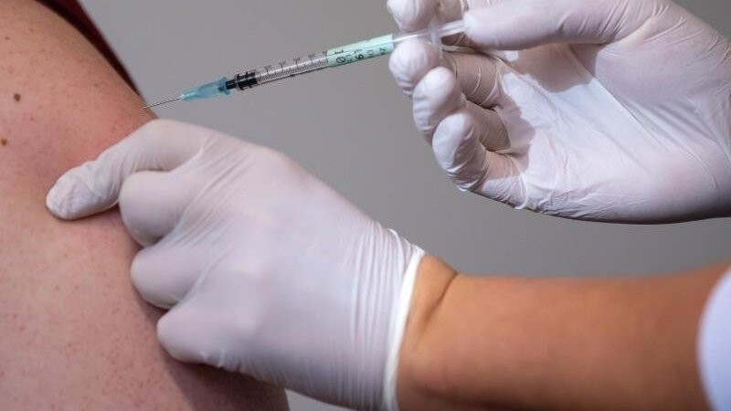 Eine Mitarbeiterin eines Impfzentrums impft einen Mann gegen Corona.