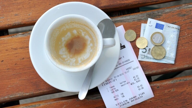 Münzen, ein Geldschein und eine Rechnung liegen neben einer leeren Kaffeetasse auf einem Tisch in einem Restaurant.