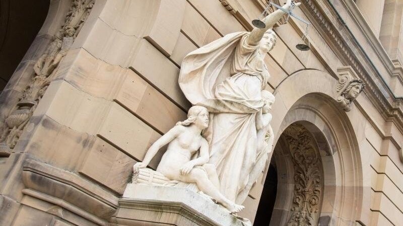 Vor einem Landgericht hält eine Statue der Justitia eine Waagschale.