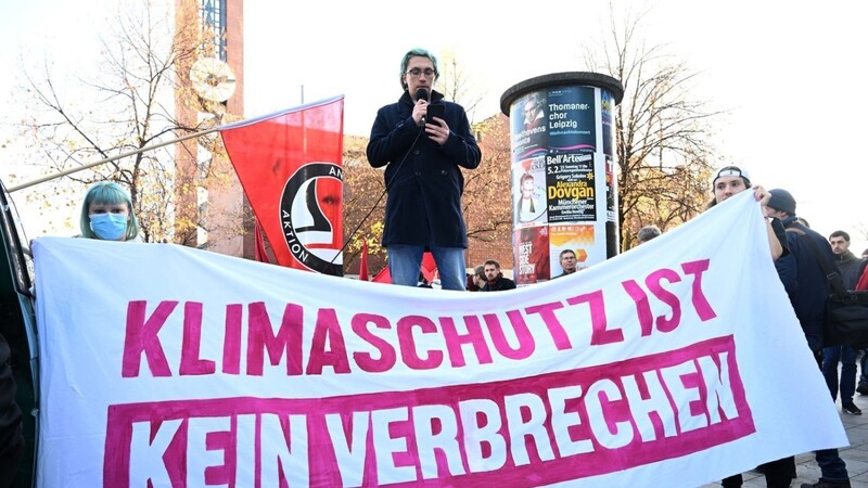 Ein Demonstrant spricht hinter einem Banner mit der Aufschrift "Klimaschutz ist kein Verbrechen".