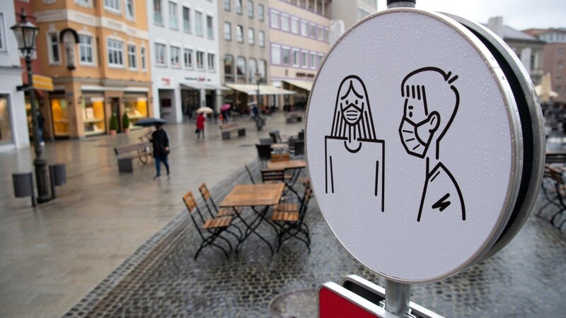 Eine symbolische Darstellung der Maskenpflicht ist auf einem Hinweisschild auf dem Rathausplatz in Augsburg zu sehen. Während dort noch kein Lockdown beschlossen wurde, gilt für den Landkreis Rottal-Inn ab Mitternacht ein Lockdown.