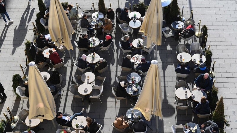 Gäste sitzen vor einem Café in der Sonne.