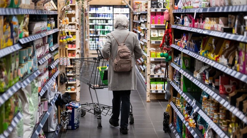 Eine Frau läuft mit ihrem Einkaufswagen durch einen Supermarkt.