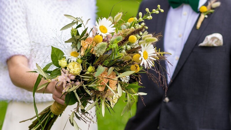 Den Brautstrauß zeigt ein Brautpaar vor seiner Trauung im Sommer. Für private Feiern gelten seit 23. August in Bayern gesonderte Regeln.