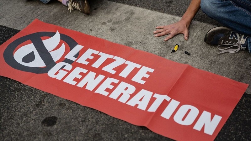 Aktivisten der Gruppe "Letzte Generation" haben sich hinter einem Banner mit ihrem Logo festgeklebt.