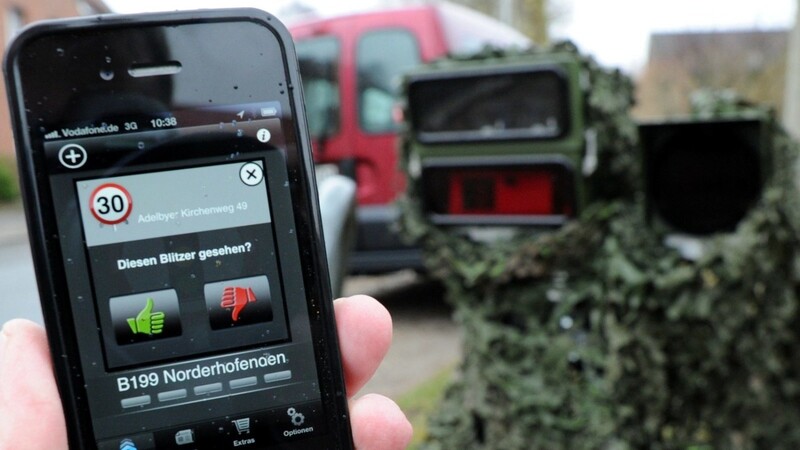 Ein Smartphone mit einer Blitzer-Warnungs-App wird am 10.04.2013 in Flensburg (Schleswig-Holstein) vor eine mobile Geschwindigkeits-Messanlage gehalten.
