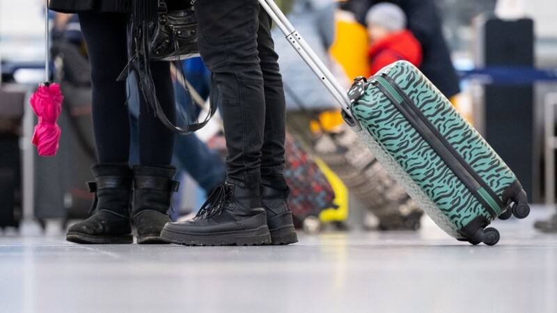 Passagiere stehen mit ihrem Gepäck an Check-in-Schaltern am Flughafen München.