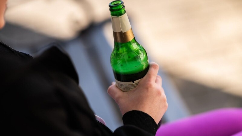 Eine Jugendliche sitzt mit einer Flasche Bier auf einer Parkbank.