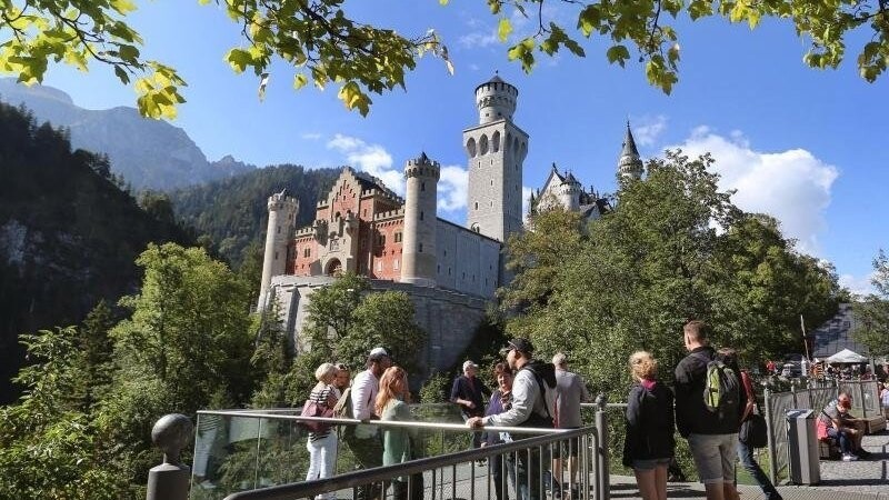 Touristen stehen an einer Aussichtsplattform unterhalb des Schlosses Neuschwanstein.