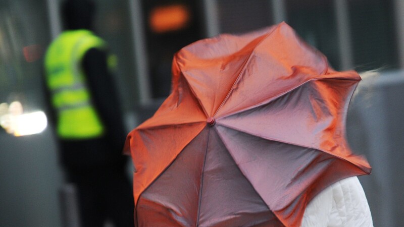 Eine Passantin stemmt sich mit einem Regenschirm gegen eine Orkanböe. (Symbolbild)