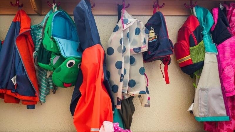 Jacken und Rucksäcke hängen an der Garderobe einer Kita. (Symbolbild).