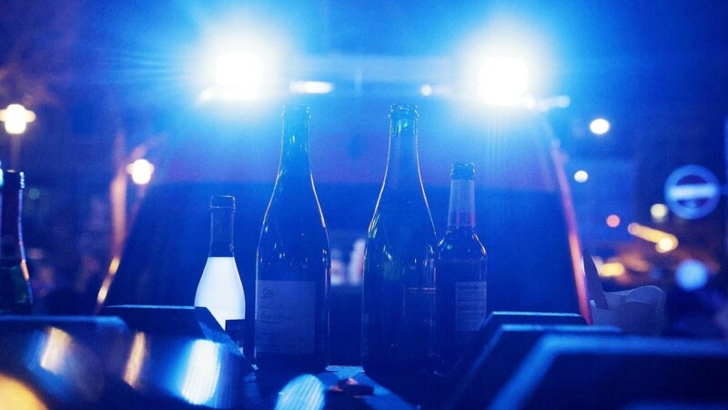 Leere Flaschen, die vorher mit alkoholischen Getränken gefüllt waren, stehen vor einem Krankenwagen mit eingeschaltetem Blaulicht.