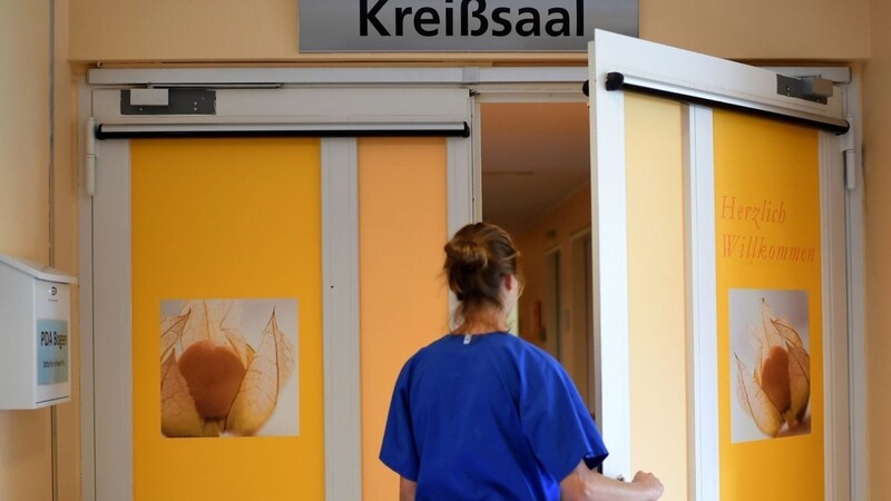 Eine Mitarbeiterin steht vor einem Kreißsaal in einem Krankenhaus.