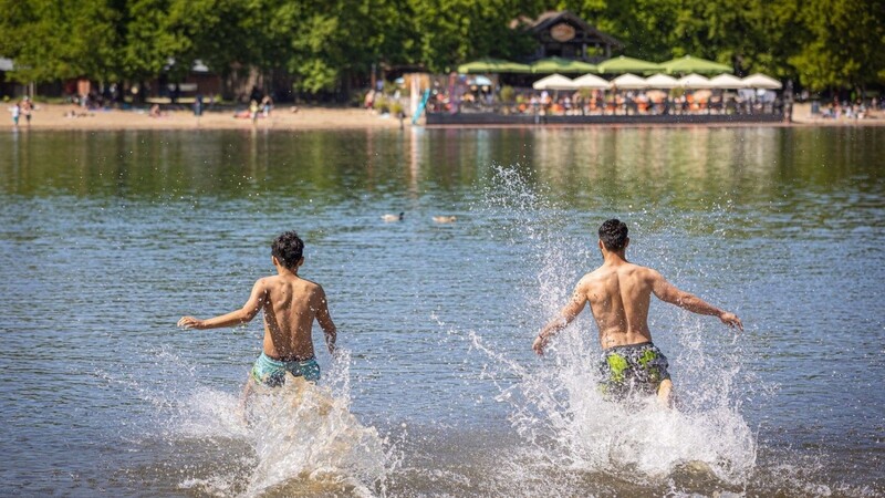 Zwei junge Männer rennen bei sonnigem Wetter in das Wasser eines Sees.