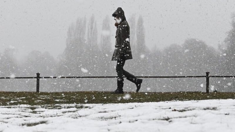Ein Frau geht bei Schneefall durch den Englischen Garten.