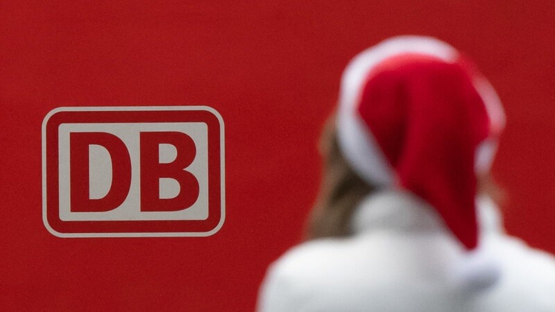 Eine Frau steht am Hauptbahnhof mit Weihnachtsmannmütze vor einem Logo der Deutschen Bahn.