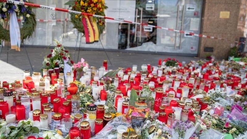 Grablichter, kerzen und Blumen liegen vor einem Kaufhaus in der Innenstadt.