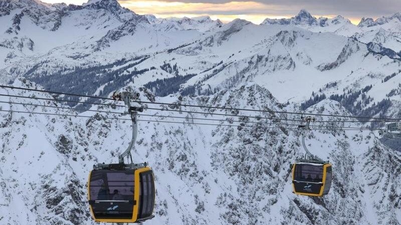 Zwei Gondeln der neuen Nebelhornbahn fahren vor dem Panorama der Alpen.