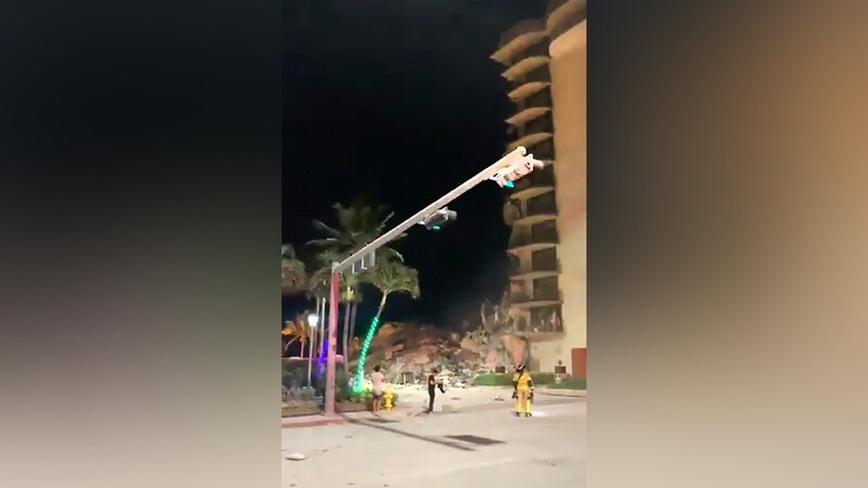 Dieses Videostandbild zeigt Menschen, die nach einem Gebäudeeinsturz auf die Trümmer schauen. Nahe Miami Beach im US-Bundesstaat Florida ist ein mehrstöckiges Wohnhaus teilweise eingestürzt. Es seien mehr als 80 Einheiten im Einsatz, teilte die Feuerwehr in der Nacht auf Twitter mit.