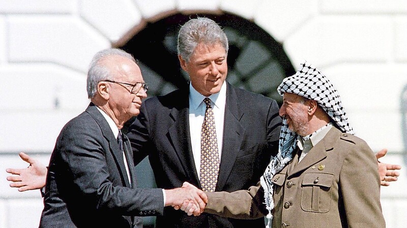 Israels Ministerpräsident Jitzchak Rabin (li.) und Yassir Arafat (PLE/PLO) reichen sich 1994 anlässlich der Unterzeichnung des Gaza-Jericho-Abkommens unter Vermittlung von Präsident Bill Clinton (Mitte) die Hand.