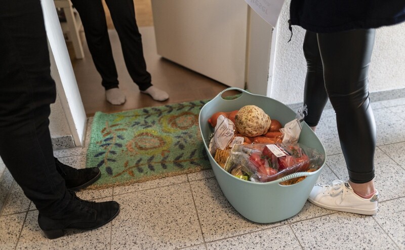 Mitarbeiterinnen eines Hilfsdienstes stehen mit Lebensmitteln vor einer Haustür. 