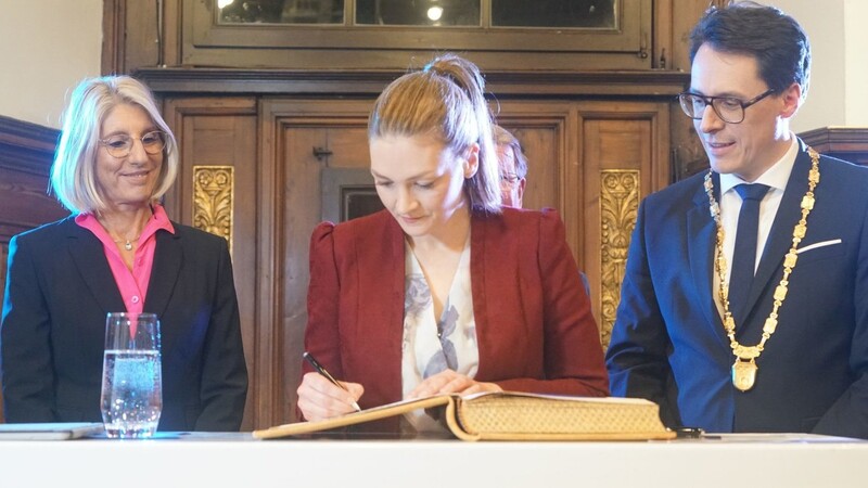 Ministerin Judith Gerlach trägt sich, flankiert von OB Moser und dritter Bürgermeisterin Renate Wasmeier, ins Goldene Buch der Stadt ein.