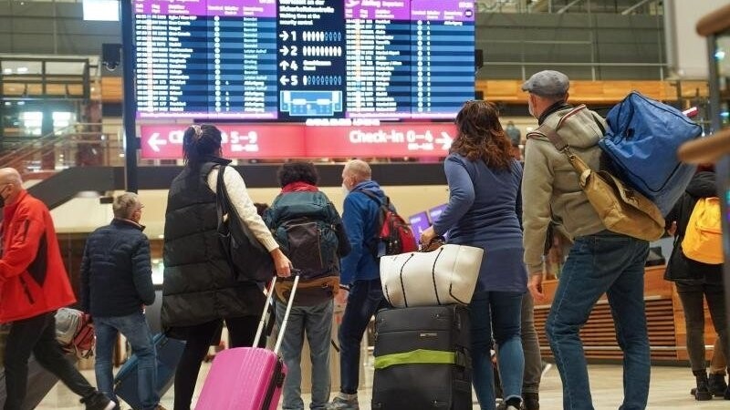 Reisende stehen am Flughafen BER vor einer Info-Tafel.