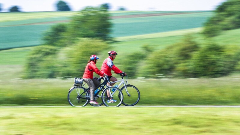 Zwei Radfahrer sind mit roten Regenjacken auf dem Donau-Radwanderweg unterwegs, der auch an Straubing vorbeiführt. Die Übernachtungsbetriebe der Stadt profitieren inzwischen kräftig von diesem beliebten Urlaubstrend.