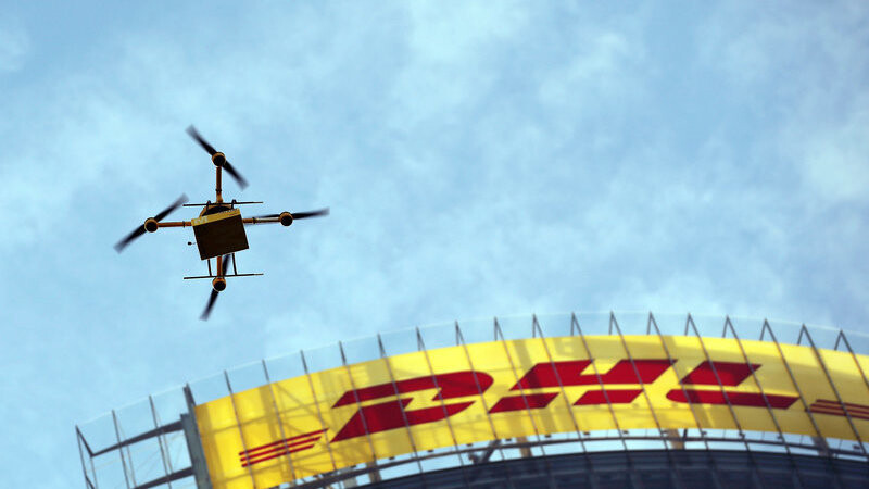 Eine Paket-Drohne der Deutschen Post DHL fliegt am 09.12.2013 in Bonn (Nordrhein-Westfalen) mit einem Paket vor dem Schriftzug der Konzernzentrale. Am 09.05.2016 teilte die DHL mit, im oberbayerischen Reit im Winkl sei die Belieferung von Paketen per Drohne erfolgreich getestet worden.