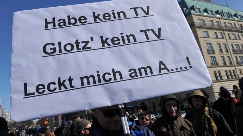 Ein Mann hält am 23.03.2013 in Berlin auf dem Pariser Platz ein Plakat mit der Aufschrift "Habe kein TV, Glotz' kein TV, Leckt mich am A....!".