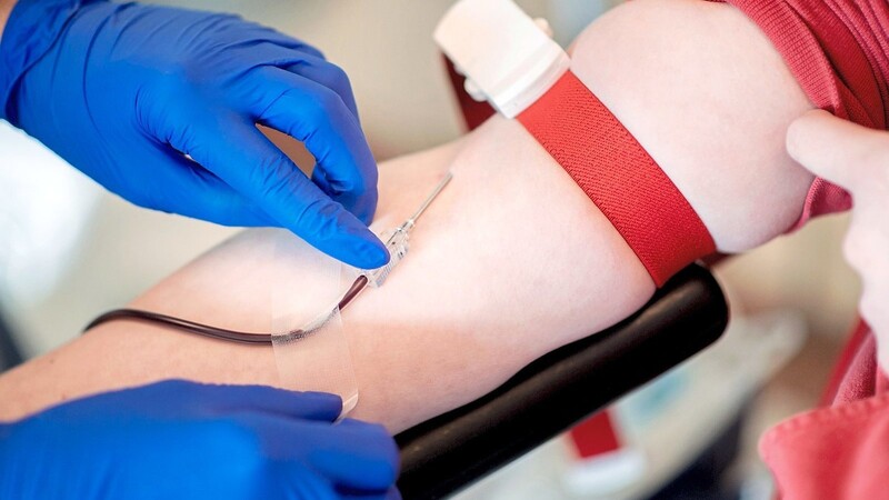 Eine Mitarbeiterin des Blutspendedienstes fixiert während einer Blutspende die Nadel.