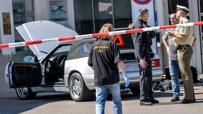 Polizisten stehen am 10.07.2015 an einer Tankstelle in Bad Windsheim (Bayern) vor dem Auto eines mutmaßlichen Amokläufers. Der 47-Jährige steht von Ende Februar an vor dem Landgericht Ansbach. Er soll eine 82 Jahre alte Frau und einen 72-jährigen Mann erschossen haben und wurde an der Tankstelle festgenommen.