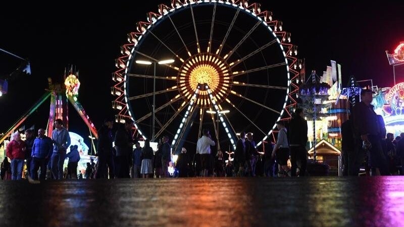 Oktoberfest 2019: Die Lichter der Wiesn und das Riesenrad spiegeln sich auf dem nassen Straße.