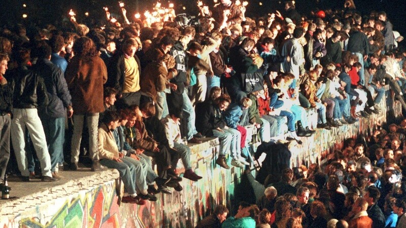 Jubelnde Menschen sitzen mit Wunderkerzen auf der Berliner Mauer am 11.11.1989. Der Mauerfall ist auch der jüngeren Generation ein Begriff. Aber sie haben eine andere Sicht auf die Einheit.