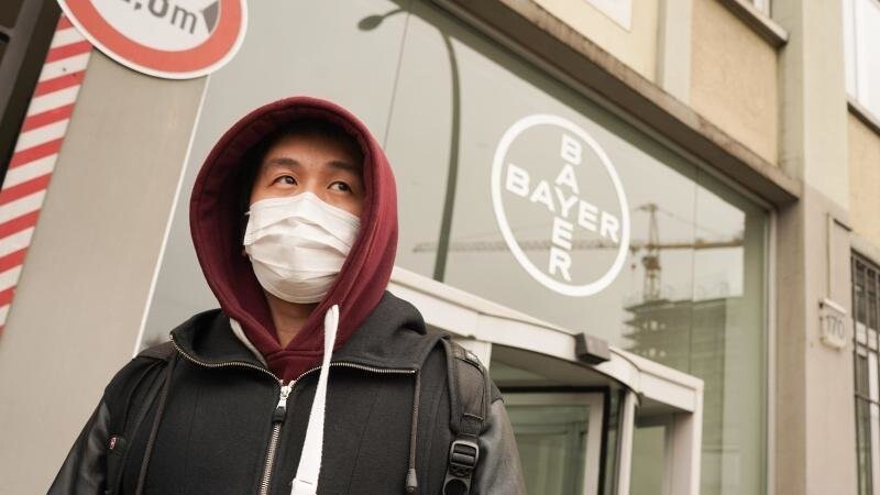 Ein Mann mit Mundschutz geht an einem Logo des Chemiekonzerns Bayer vorbei.