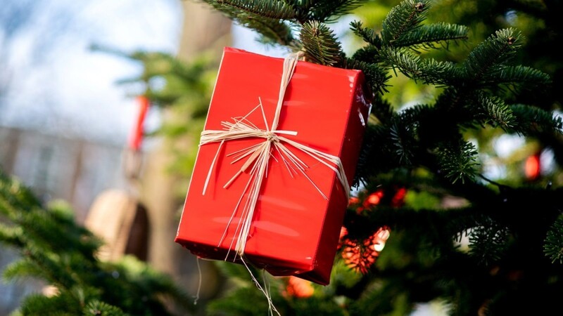 Ein Geschenk hängt an einem Tannenbaum. Woher kommt denn die Schenkerei überhaupt?