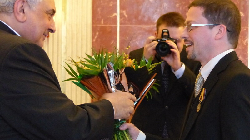 Zu der Medaille gab es für jeden der Autoren, hier Dr. Dominik Reither (rechts), vom Botschafter auch einen Blumenstrauß.